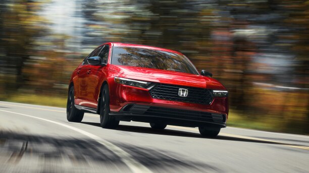 3/4 front view of red Accord, driving toward camera, taking a turn on a temperate rainforest highway in the day.