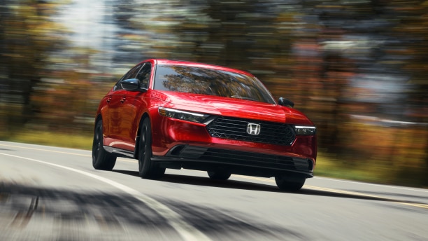 3/4 front view of red Accord, driving toward camera, taking a turn on a temperate rainforest highway in the day.