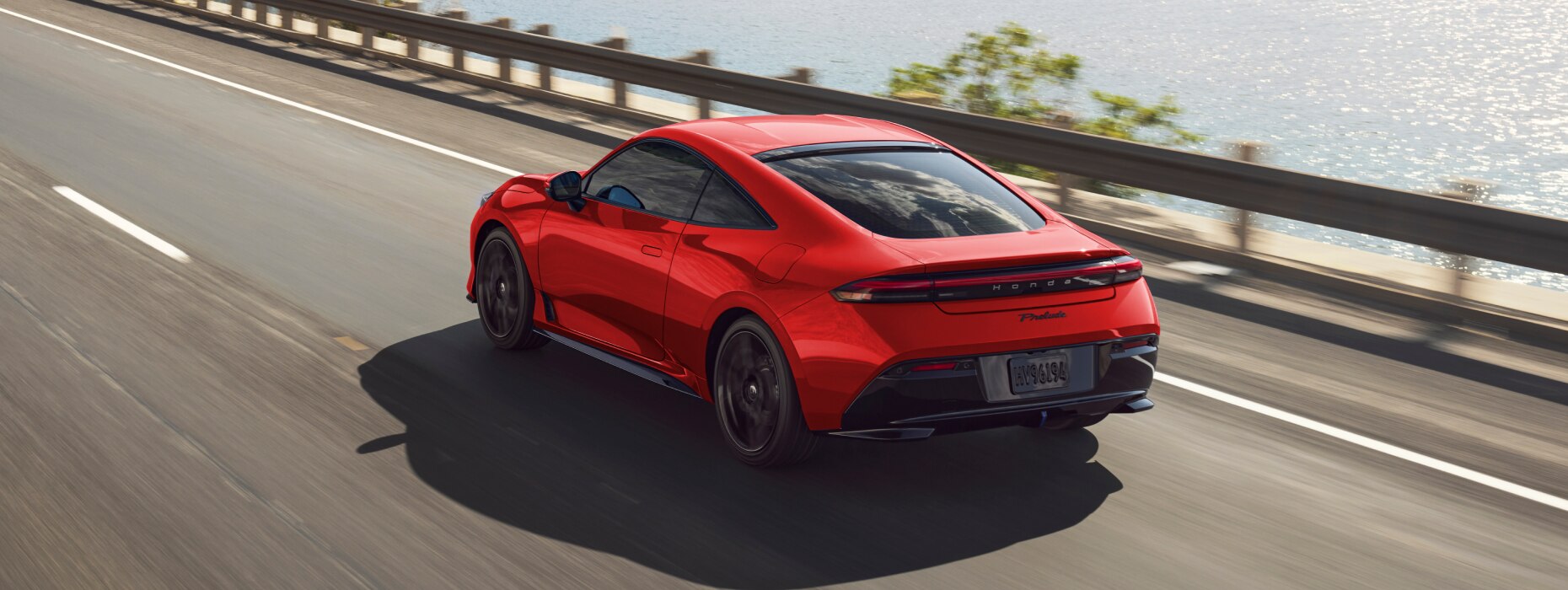 Rear view of a red Prelude driving down a coastal highway. 