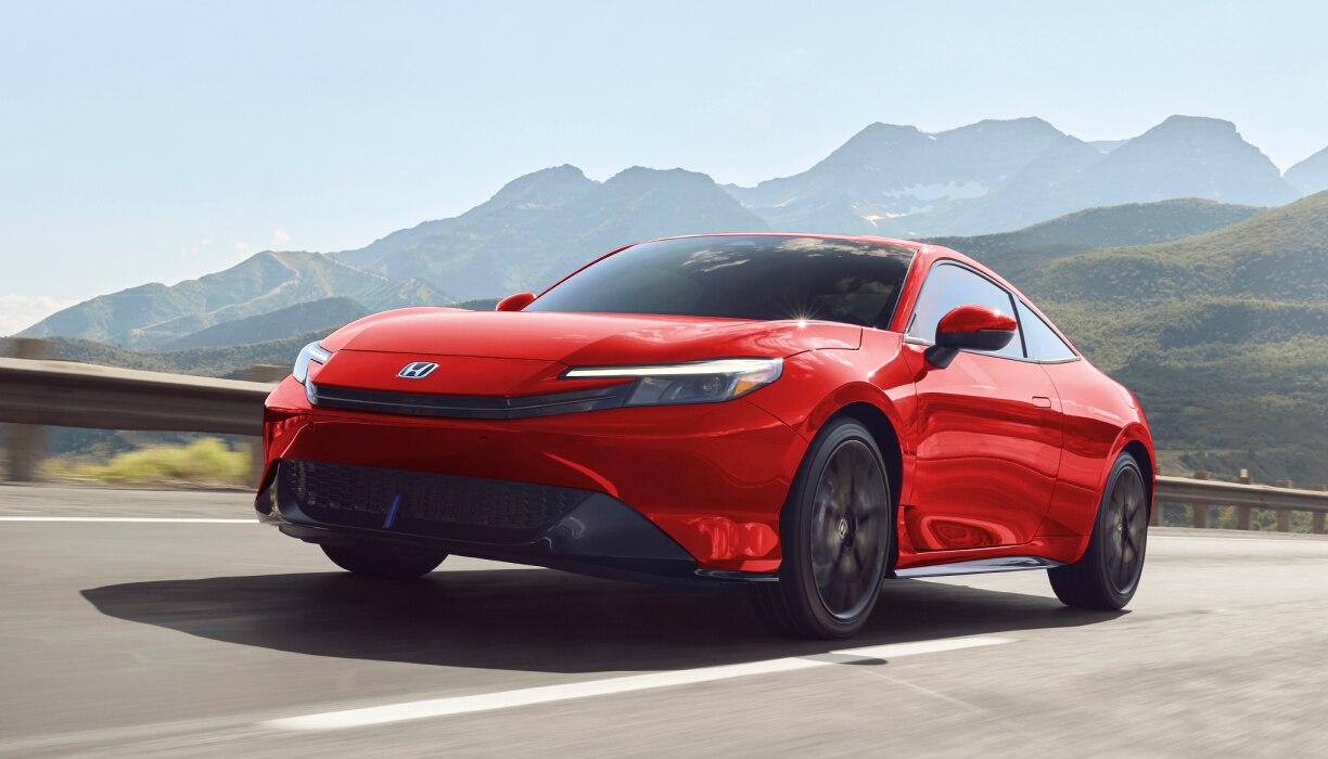 Front-view of a red prelude driving along a coastal highway. 