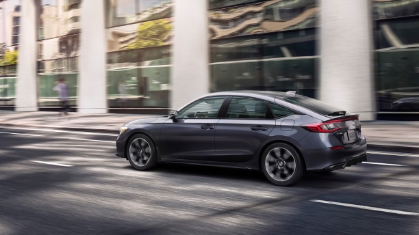 Side view of grey Hatchback driving on a city street.