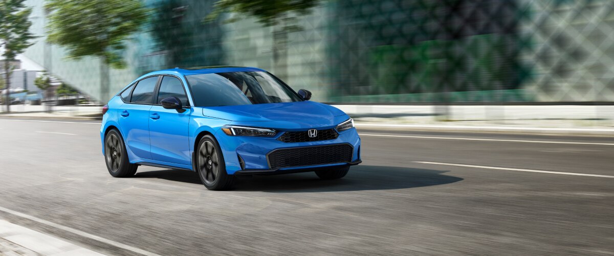 Front view of a blue hatchback as it drives on a city street.