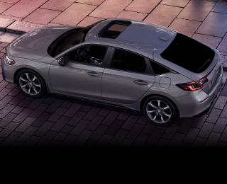 3/4 bird’s eye view of grey Hatchback parked on brick city road.