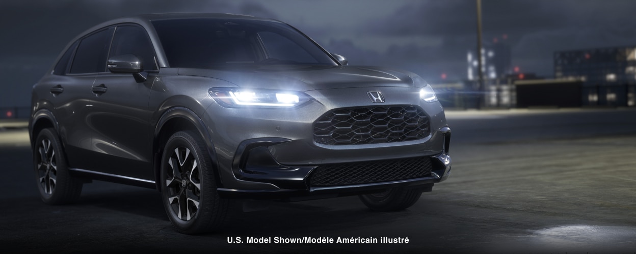3/4 front view of a grey HR-V parked on rooftop parking lot at night with LED headlights on.