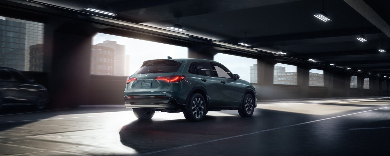 3/4 rear view of an HR-V in Nordic Forest Pearl colour driving in an empty parking garage.