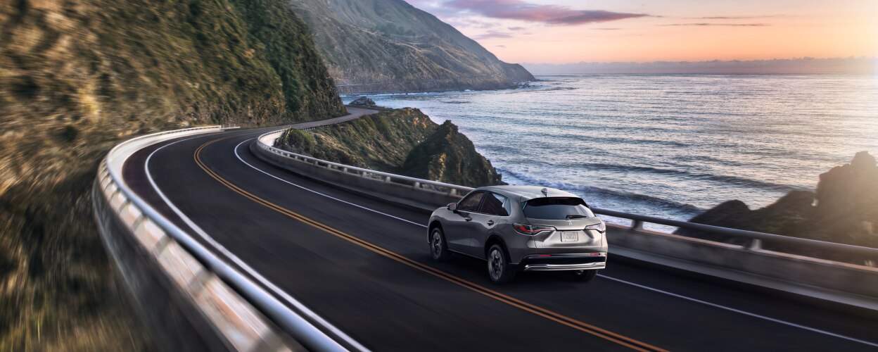 3/4 rear view of a grey HR-V driving on coastal highway.