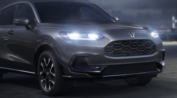 3/4 front view of a grey HR-V parked on rooftop parking lot at night with LED headlights on.