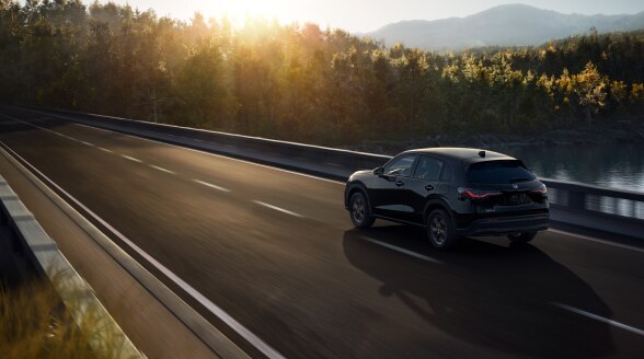 3/4 rear view of black HR-V driving on a bridge over a lake. 