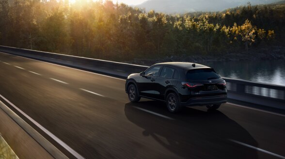 3/4 rear view of black HR-V driving on a bridge over a lake. 