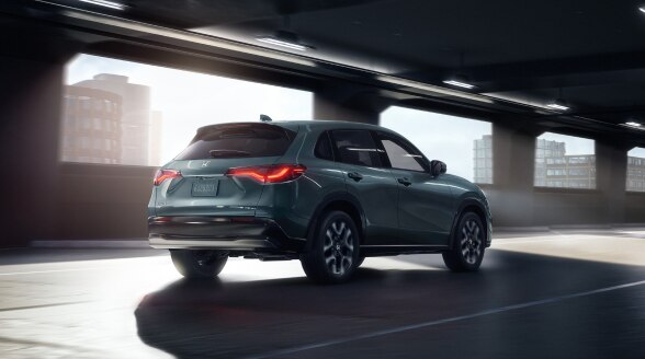 3/4 rear view of an HR-V in Nordic Forest Pearl colour driving in an empty parking garage.