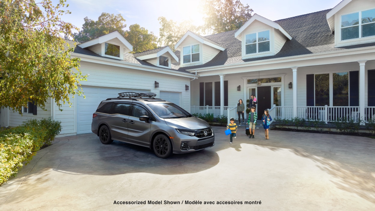 3/4 front side view of grey Odyssey parked in driveway. Family walking toward it.