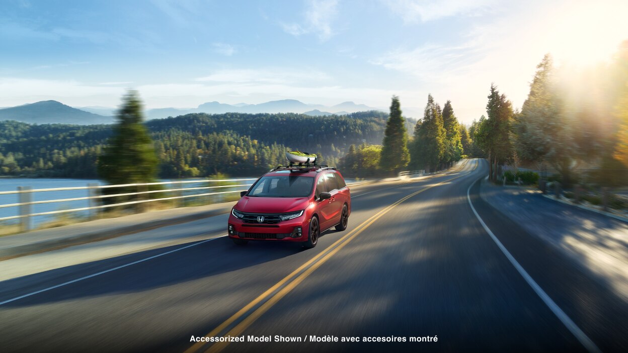 3/4 front view of red Odyssey driving on lakeside road.