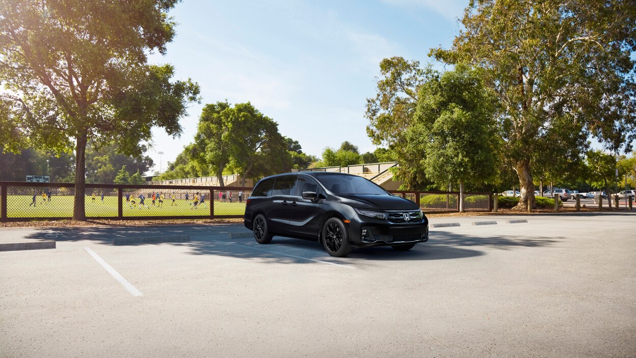3/4 front view of black Odyssey parked by a soccer field.