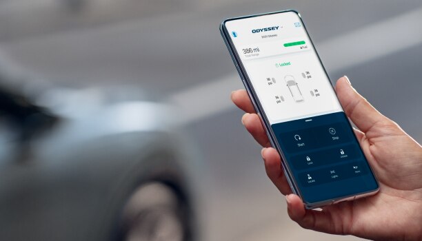 Hands using HondaLink app on phone. Grey odyssey parked in the background.  