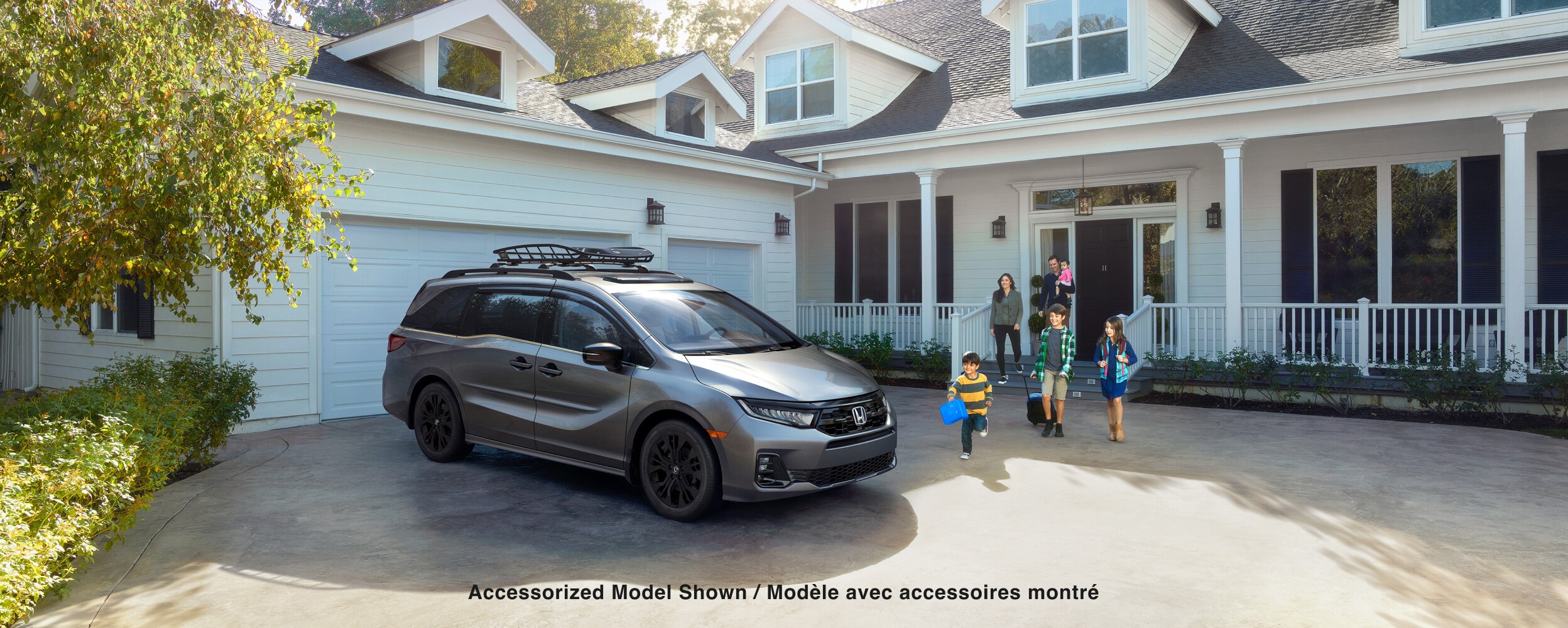 3/4 front side view of grey Odyssey parked in driveway. Family walking toward it.