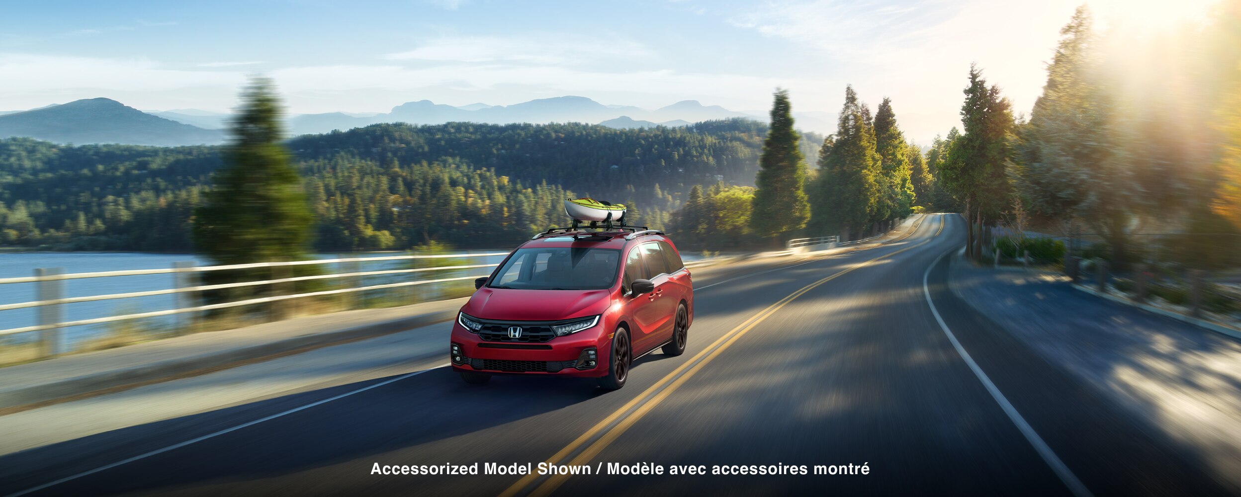 3/4 front view of red Odyssey driving on lakeside road.