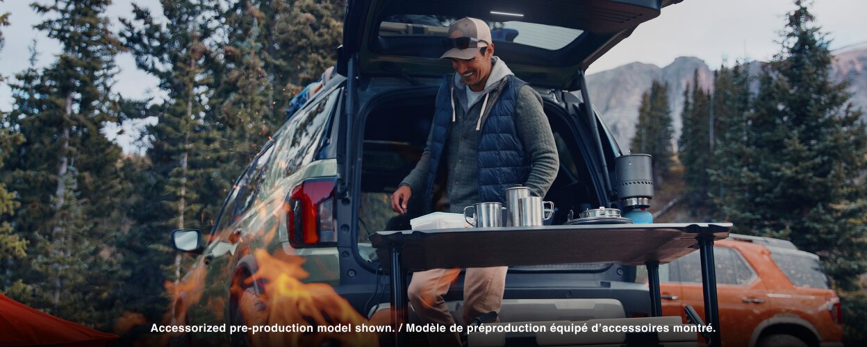 A man sets up a camping cookout behind a Passport. 