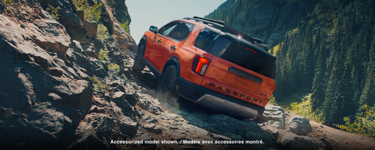 Rear-view of an orange Passport driving on rough mountain terrain. 