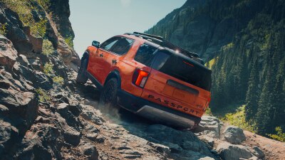 A Honda Passport is depicted drving up a steep incline. 
