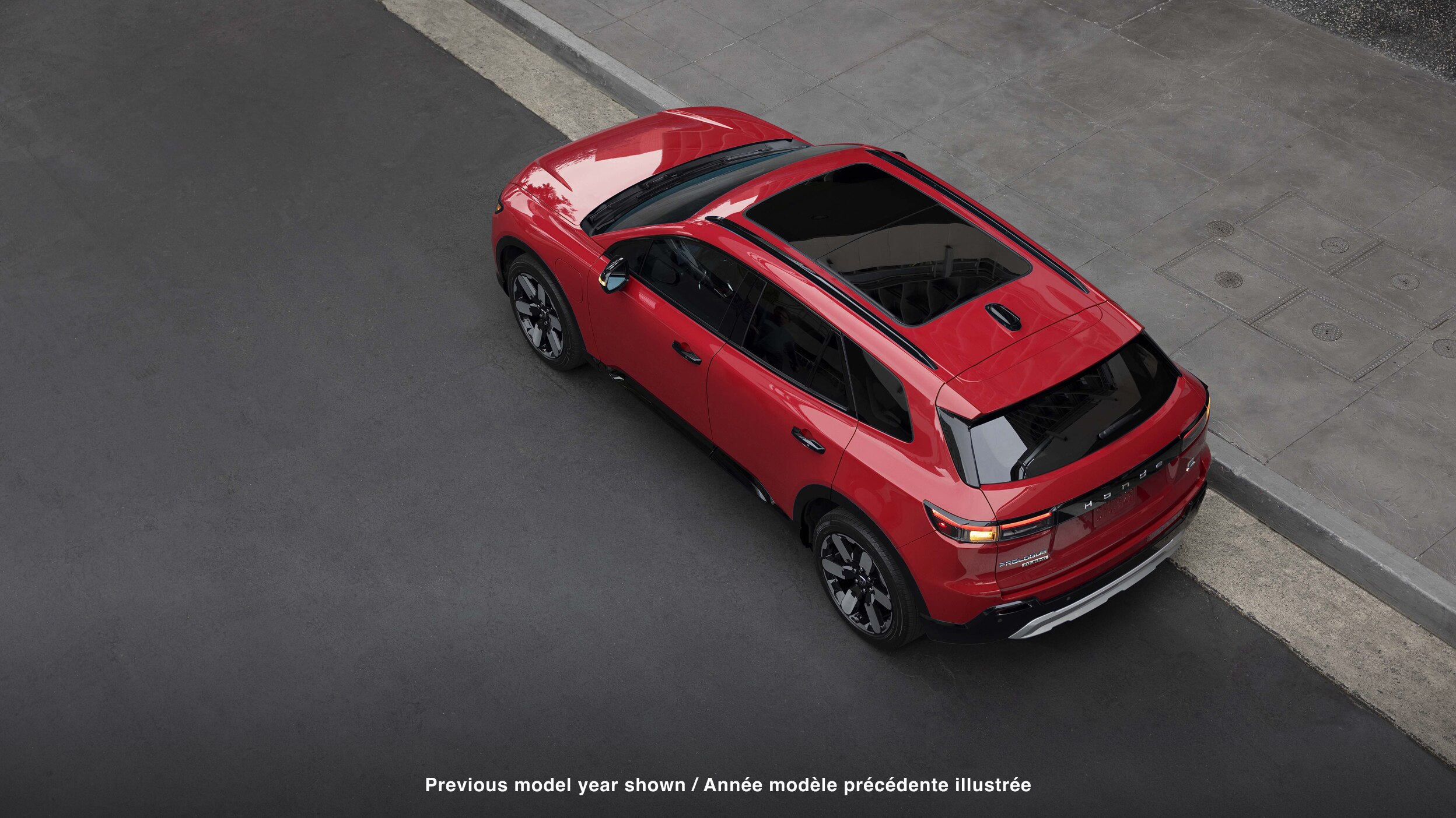 3/4 rear bird's eye view of red Prologue parked curbside on a city street. 