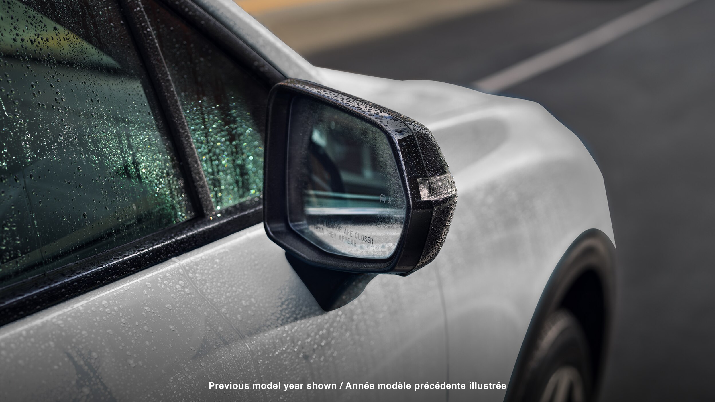 Closeup of side mirror on white Prologue covered in rain drops. 
