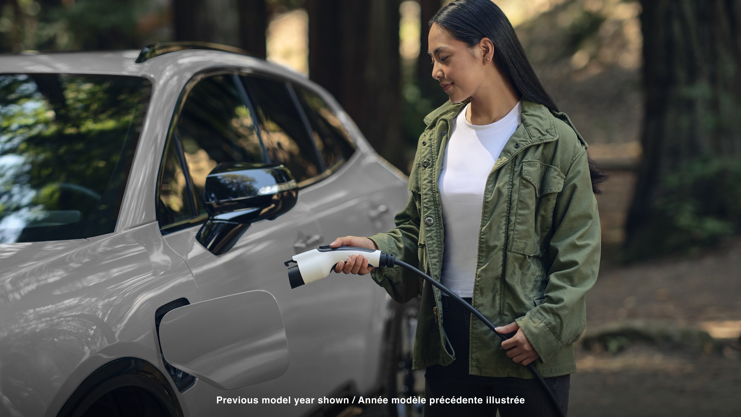 View of a woman plugging in a charging cord into a white Prologue in temperate forest.