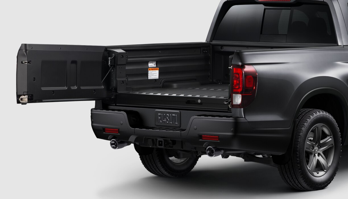 3/4 rear view of black Ridgeline on white space. Tailgate open to the side.