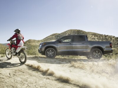 Side view of grey Ridgeline on desert hills with motocrosser on the left.
