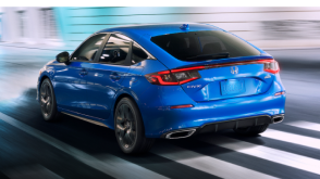 3/4 medium closeup of blue Hatchback driving on well-lit city street at night.