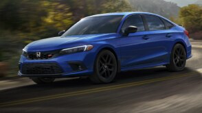 3/4 front side view of blue Civic Si taking a turn on a mountain highway.