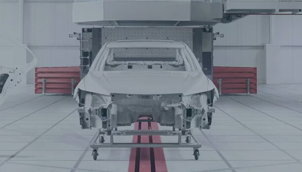 The frame of a Honda vehicle is on a lift inside an white industrial space.  