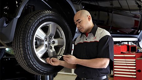 Image of a Honda technician using equipment to check and maintain tire pressure on a black Honda in a workshop setting. // Image d'un technicien Honda utilisant un équipement pour vérifier et maintenir la pression des pneus d'une Honda noire dans un atelier.